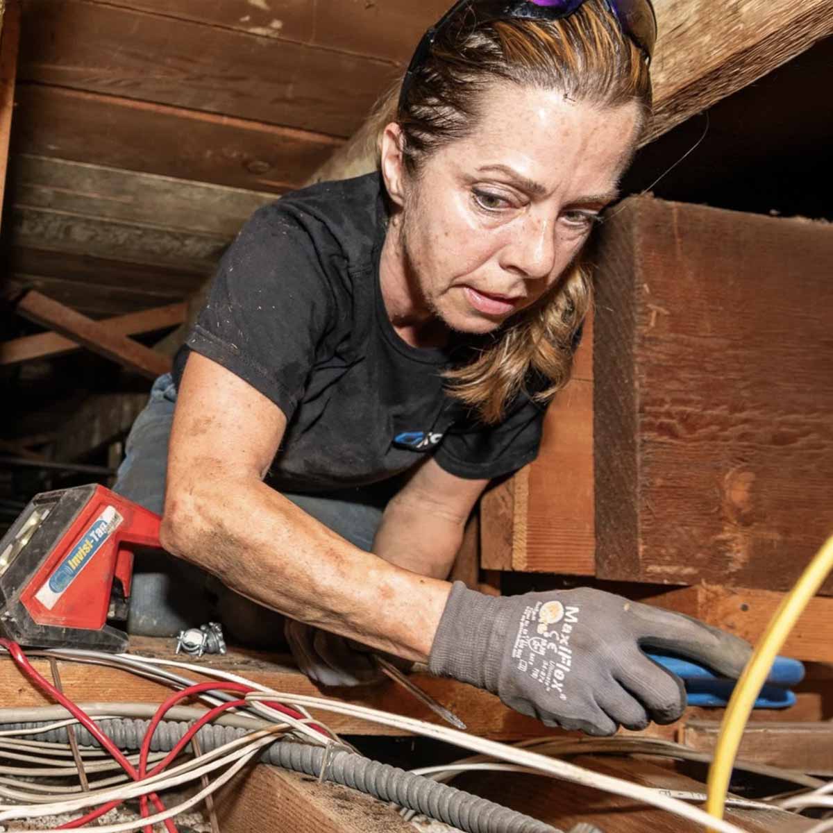 Woman electrician in the attic working on wires.