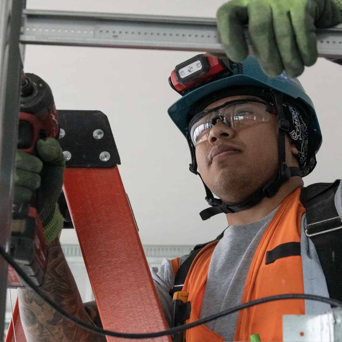 Electrician Trainee working with a drill on a ladder.
