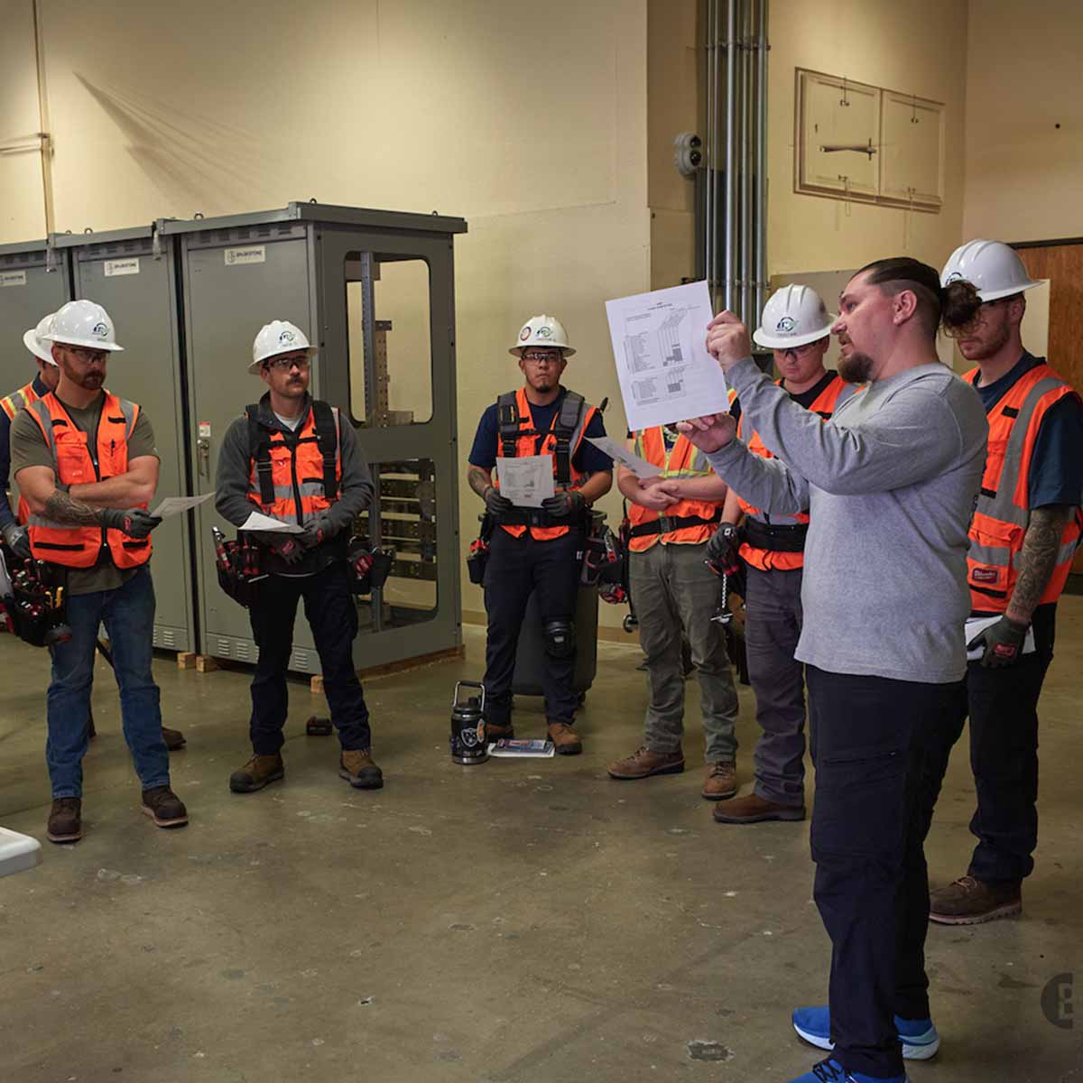 Instructon pointout instructions on paper with Electrician Trainees holding the same paper.