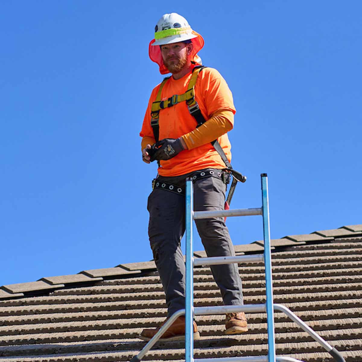Electrician Trainee on a roof about to use a ladder to get down.